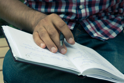 Close-up shot: the hand of a young migrant. He is making notes in a diary.