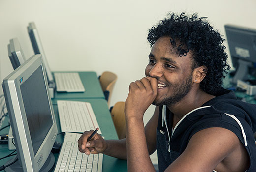 Tsegazgi Berhe sitting at a computer. He is smiling.